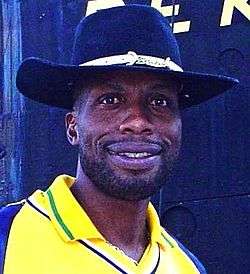 A black man in a wide-brimmed hat, wearing a yellow shirt