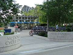 Opposing stone entrances saying "McDonald's Cycle Center" and "Millennium Park" in front of parked bicycles and a two-story glass building