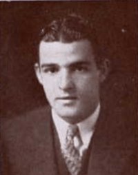 Man sitting in suit and tie, with hair parted.