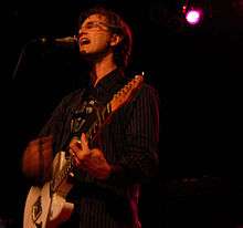 A picture of a man singing and playing a guitar