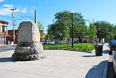 A large stone block with "Dana Memorial" carved into the top and a water basin on the side facing the viewer. It is on a narrow strip of sidewalk in an urban area with a grassy area planted with trees behind it.