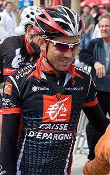 A road racing cyclist in a black and red jersey with white trim, and a matching helmet.
