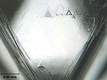 A triangular facet of a crystal having triangular etch pits with the largest having a base length of about 0.2 millimetres (0.0079 in)