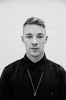 Diplo looking down wearing a blue and yellow headphone