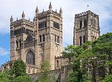 The two square front towers of a cathedral rising above some trees. Behind the paired towers is another taller square tower.