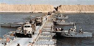 Military trucks crossing a canal on a pontoon bridge