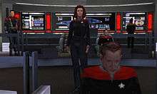 A computer-rendered version of the bridge featured in Star Trek: Voyager. A woman gives orders from the center of the room, while a man works on a console in the foreground. The ship's executive officer sits in a chair to the right, and a crewman works on a panel with the ship's schematics in the background. To the left, a man in an armored uniform watches the activity.