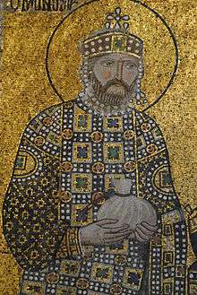A mosaic with a background of gold showing a bearded man wearing a crown and jeweled robes holding a small bag in his hands which is tied at the top