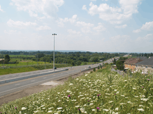 A freeway changes into a four lanes conventional road, and vanishes into the rural foothills