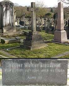 A tall granite headstone in the shape of a cross, surrounded by other graves