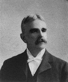 A man with graying hair and a mustache wearing a black jacket and vest and white shirt and bowtie