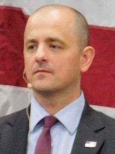 McMullin, wearing a microphone, in front of the red and white stripes of a U.S. flag