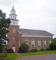 A side view of the church on an overcast day with the steeple at left. On the main block are five round-arched windows similar to those on the steeple