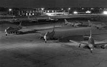 Jets lined up on a concrete ramp with buildings seen in the background