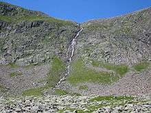 Water streaming down rocky hill with bare landscape save for patches of grass