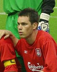 Head and upper torso of a young dark-haired white man wearing a red football shirt bearing the Carlsberg logo.