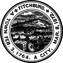  A black and white circular seal with a group of gears and mechanical parts in the foreground and a hill with a rock on the top in the background.