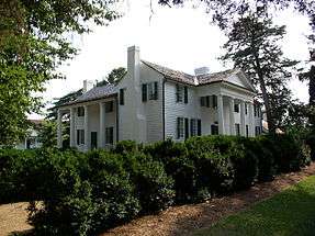 Large, classic style white house surrounded by lots of greenery.