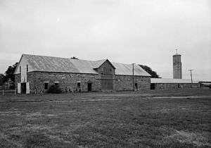 A black and white picture of a long two story Quartermaster store building made of yellowish cut stone with a wooden second floor. The building is in the style of the late 1860s.