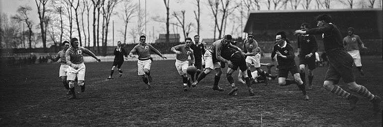 A rugby match with players from both teams bearing down on a loose ball