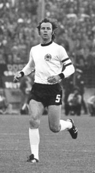 A black-and-white photograph of a dark-haired soccer player in white shirt, black shorts and white socks running towards the viewer.