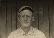 A black and white head shot of a man in a baseball cap.