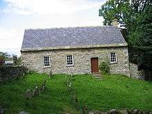 A small, stone, single-storey building with a slate roof in a burial ground with gravestones. Seen from the front, it has steps leading up to a door and three windows.