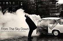 A black-and-white image of Larry Mullen, Jr. in front of a large cloud of smoke coming from a car. He is staring upwards with his body arched backward. The title "From the Sky Down" is written on the left, with film credits below.