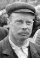 Fuzzy head-and-shoulders photo of a 40-year-old man in a cloth cap and mustache