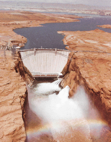Glen Canyon Dam releasing floodwater. A rainbow is visible over the Colorado River.