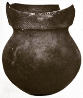 Black and white photo of a ceramic pot with a round bottom, short neck, and a rim decorated with geometric line patterns. The rim is broken in the rear.
