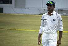 A man in the Indian test cricket uniform standing near the boundary line
