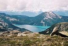 A mountain rising above a lake in the foreground with glaciated mountains in the background.