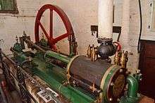 Green painted machinery with a horizontal shaft and wheel behind