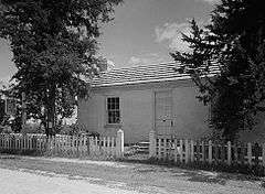 A small home with a picket fence in front, between two trees, in black-and-white.