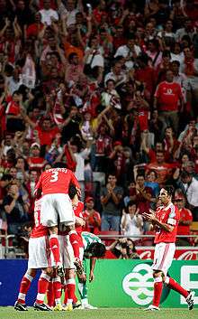 Players celebrating a goal in front of  fans wearing red, the team color