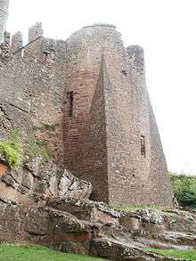 A massive castle tower, sat on top of a rugged rock outcrop; a massive angular stone spur juts out from the base of the tower towards the viewer.