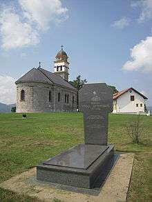 a grey polished stone grave with a stone-walled church in the background