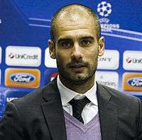 Josep Guardiola is seen in the picture. He is shown with a faded beard and hair wearing a suit.