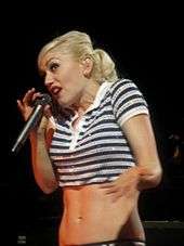 A blonde woman wearing a black and white-striped top singing into a microphone