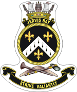 A ship's badge. A naval crown sits on top of a black scroll with "JERVIS BAY" written in gold. This is atop a yellow, rope-patterned ring, which contains a black field. Three gold fleur de lys are positioned at the bottom, upper left, and upper right: the bottom one is separated from the other two by a white chevron containing eight black marks. Below the ring are a stone axe and a nulla nulla sitting on top of a boomerang. At the bottom of the badge is a black scroll with "STRIVE VALIANTLY" written.