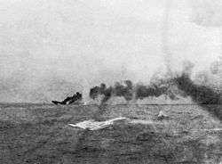 A large ship is sinking in the distance; a large dense cloud of smoke emanates from the wreck.