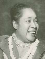 A smiling woman with a topknot and strings of shells around her neck