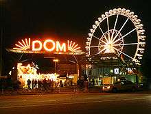 A red lighted sign with the word Dom and a lighted Ferris wheel in the background.