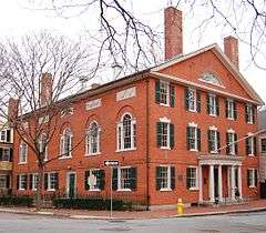 A large rectangular two story hall made of brick. The long side has five large windows topped with a rounded window section, while the short side has more conventionally sized windows.