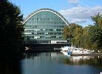 A body of water with a multi-storey office building whose outline forms an arc.