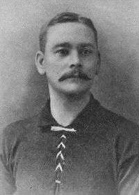 Head and upper torso of a white man with a moustache wearing a dark sports shirt.
