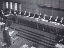 One man at a lectern addressing a large panel of judges