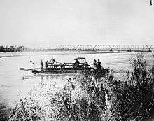 Ferry on the Salt River carrying a horse and buggy. Railroad bridge seen in the background.