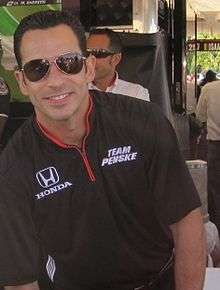 Man in his mid thirties smiling at the camera. He is wearing a black T-shirt and sunglasses.